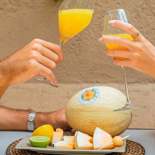 Pareja celebrando y brindando con una copa de zumo con melón Waikiki. Sorprende.
